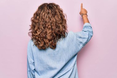 Orta yaşlı güzel bir kadın pembe arka planda duran sıradan bir kot gömlek giyiyor.