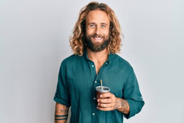 Sakallı, uzun saçlı, içki arkadaşı aşılamalı. Pozitif ve mutlu görünüyor. Kendine güvenen bir gülümsemeyle dişlerini gösteriyor. 