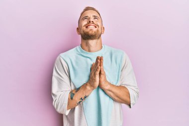 Kafkasyalı genç bir adam gündelik giysiler giyiyor. Elleriyle yalvarıyor ve dua ediyor. Yüzünde umut ifadesi var. Yalvarıyor. 