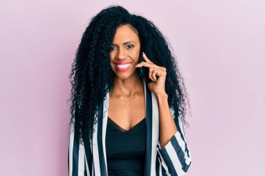 Orta yaşlı Afro-Amerikalı kadın akıllı telefondan konuşuyor. Olumlu ve mutlu görünüyor. Kendine güvenen bir gülümsemeyle dişlerini gösteriyor. 