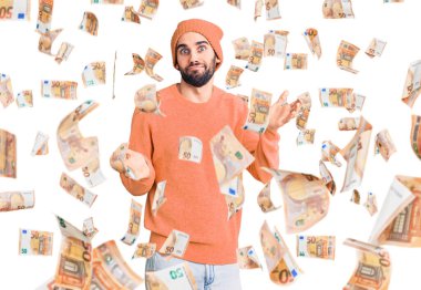 Sakallı, günlük kazaklı, yün şapkalı, kafası karışık, elleri ve kolları havada genç yakışıklı bir adam. şüphe kavramı.