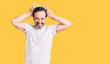 Orta yaşlı yakışıklı bir adam günlük tişört giyiyor komik ve deli pozu veriyor parmakları tavşan kulağı gibi, neşeli gülümsüyor. 