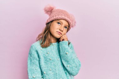 Yün kazak giyen güzel bir kız ve güzel bir şapkası var. Kuşkuya odaklanmış, çenesine parmak geçirmiş ve kafasını kaldırıp merak ediyor. 