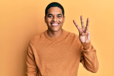 Genç, yakışıklı, sıradan bir süveter giyen, üç numaralı parmaklarını gösterip, gülümseyen, kendinden emin ve mutlu bir İspanyol.. 