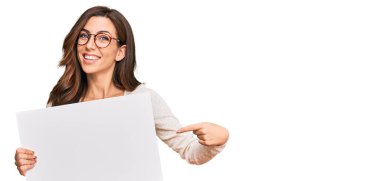 Boş afiş tutan genç esmer kadın mutlu bir şekilde el ve parmak işareti yapıyor. 