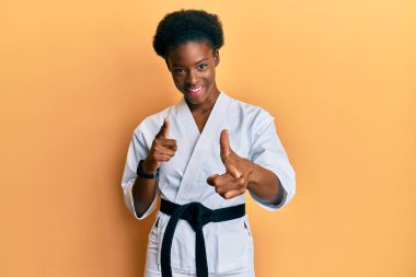 Karate kimonosu ve siyah kuşak giyen genç Afrikalı Amerikalı kız kamerayı mutlu ve komik yüzüyle işaret ediyor. iyi enerji ve titreşimler. 