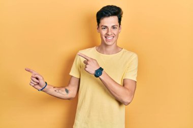 Gündelik sarı tişört giyen genç İspanyol adam gülümsüyor ve kameraya bakıyor iki eliyle ve parmaklarıyla kenarı işaret ediyor.. 