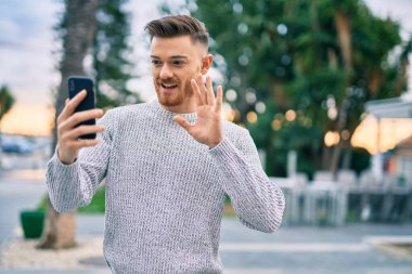 Kafkasyalı genç adam şehirde akıllı telefon kullanarak video araması yaparken mutlu gülümsüyor..