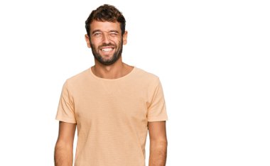 Sakallı, sıradan tişörtlü yakışıklı bir genç. Seksi bir ifadeyle kameraya bakıyor. Neşeli ve mutlu bir yüzü var.. 