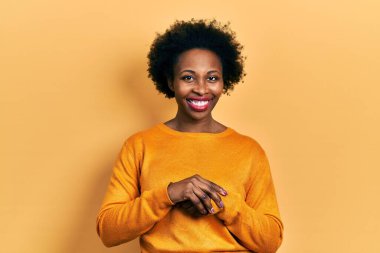 Genç Afro-Amerikalı kadın, günlük kıyafetler giyip ellerini birleştiriyor ve mutlu bir şekilde gülümsüyor. Başarı ve iyimserlik 