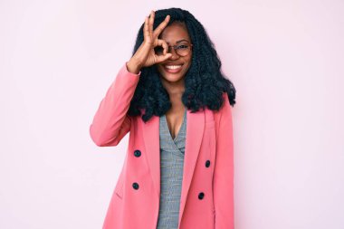 İş ceketi ve gözlük takan güzel bir Afrikalı kadın el hareketleriyle gülümsüyor ve mutlu yüzüyle parmaklarının arasından bakıyor.. 