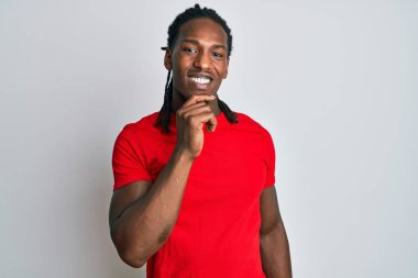 Saçları örgülü Afrikalı Amerikalı bir adam kameraya kendinden emin bakıyor kollarını kavuşturmuş ve çenesini kaldırmış gülümsüyor. Olumlu düşünmek. 