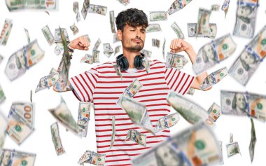 Genç İspanyol adam kulaklık kullanarak müzik dinliyor ve gururla gülümseyen kol kaslarını gösteriyor. fitness konsepti.