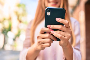 Genç beyaz kız şehirde akıllı telefon kullanarak mutlu bir şekilde gülümsüyor..