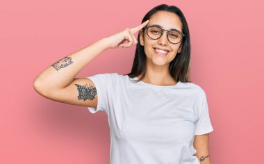 Gündelik beyaz tişört giyen genç İspanyol kadın tek parmakla başını işaret ediyor, harika bir fikir ya da düşünce, iyi bir hafıza. 