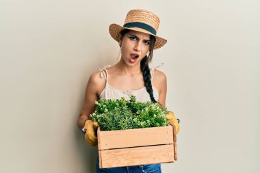 Genç İspanyol kadın yeşil saksıyı şok suratıyla tutuyor, şüpheci ve alaycı görünüyor, ağzı açık kalınca şaşırıyor. 