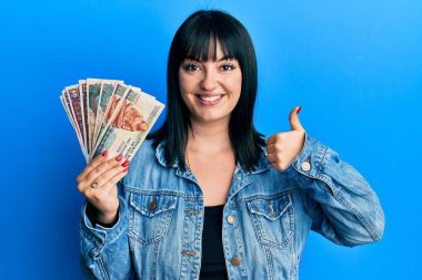 Genç İspanyol kadın elinde Mısırlı banknotlar tutuyor mutlu ve pozitif gülümsüyor, başparmağıyla mükemmel ve onay işareti yapıyor. 