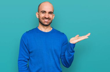 Gündelik kıyafetler giyen genç İspanyol adam neşeli bir şekilde gülümsüyor ve avuç içi kameraya bakıyor.. 