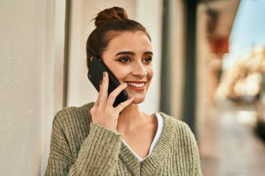 Güneşli bir sonbahar gününde, mutlu ve kendinden emin bir şekilde gülümseyen güzel esmer kadın telefonda konuşuyor.