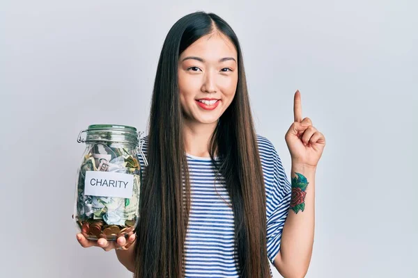 Mladá Číňanka Držící Charitativní Sklenici Penězi Usmívající Nápadem Nebo Otázkou — Stock fotografie