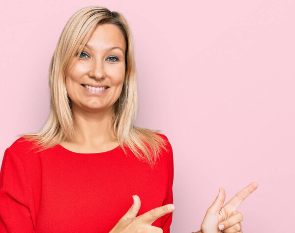 Кавказская женщина средних лет в повседневной одежде улыбается и смотрит в камеру, указывая двумя руками и пальцами в сторону.. 