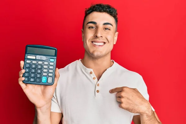 Jovem Hispânico Mostrando Dispositivo Calculadora Apontando Dedo Para Auto Sorrindo — Fotografia de Stock