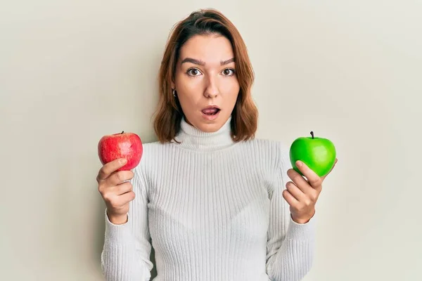 年轻的高加索女人手里拿着红绿相间的苹果 既害怕又惊讶 脸上充满了惊奇 恐惧和兴奋 — 图库照片