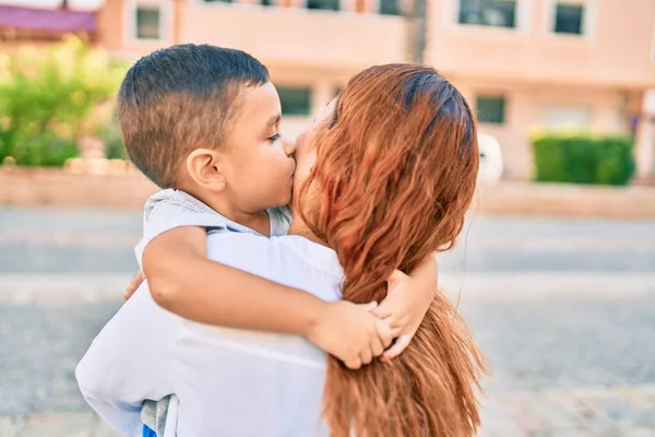 Adorable latin mother and son smiling happy hugging and kissing at the city.