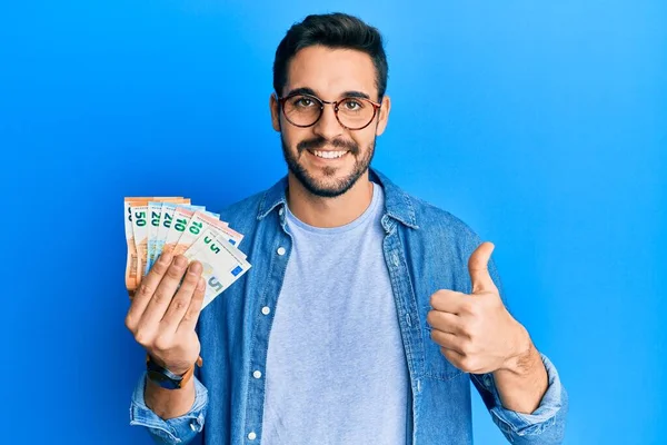 Joven Hispano Sosteniendo Billetes Euros Sonriendo Feliz Positivo Pulgar Hacia — Foto de Stock