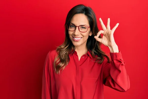 カジュアルな服と眼鏡を身に着けている若いラテン語の女性は 手と指でOkサインを行う積極的な笑顔 成功した表現 — ストック写真