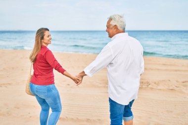 Orta yaşlı İspanyol çift kumsalda yürürken mutlu bir şekilde gülümsüyor..