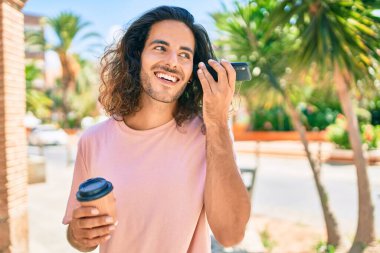 Genç İspanyol adam gülümsüyor. Akıllı telefonla konuşuyor ve şehirde kahve içiyor..