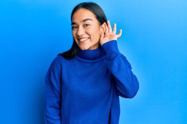 Asyalı genç bir kadın, günlük kışlık süveter giyiyor. Kulağından kulaklarına gülümseyerek dedikodu ve dedikoduları dinliyor. Sağırlık kavramı. 