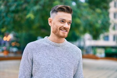 Genç beyaz adam parkta mutlu bir şekilde gülümsüyor..