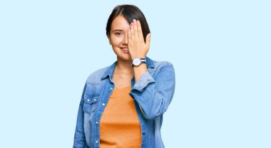 Kısa saçlı, güzel İspanyol bir kadın. Sıradan bir kot ceket giyiyor. Bir gözünü eliyle kapatıyor.. 