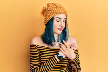 Genç modern kız yün şapka takıyor, elleri göğsünde, gözleri kapalı gülümsüyor ve yüzünde minnet ifadesi var. sağlık kavramı. 