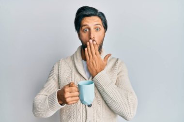 Genç İspanyol bir adam bir fincan kahve içiyor. Ağzını eliyle kapatıyor. Şok geçiriyor ve hata yapmaktan korkuyor. şaşırmış ifade 