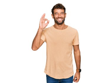 Sakallı, rahat tişörtlü, gülümseyen ve el ve parmaklarıyla 