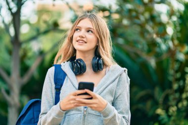 Parkta akıllı telefon kullanarak gülümseyen güzel beyaz öğrenci.