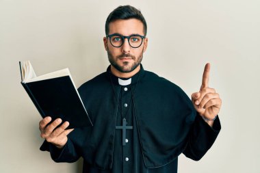 İncil 'i elinde tutan genç İspanyol rahip yüzünde ciddi bir ifadeyle rahatlamış. Basit ve doğal bir şekilde kameraya bakıyorsun.. 