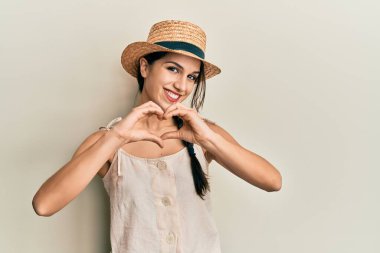 Yaz şapkası takan, aşık gülümseyen, elleriyle kalp sembolü yapan genç İspanyol kadın. romantik kavram. 