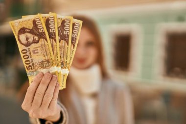 Genç kızıl saçlı kız gülümsüyor. Şehirde Macar banknotları tutuyor..