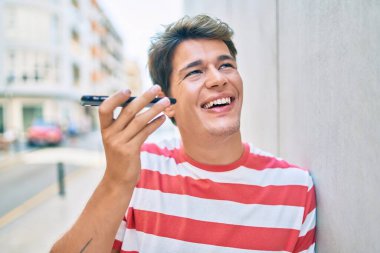 Genç beyaz adam gülümsüyor. Şehirdeki akıllı telefonu kullanarak sesli mesaj gönderiyor..