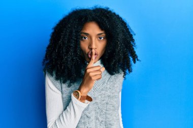 Afro saçlı, kışlık süveter giyen, dudakları parmaklı Afro-Amerikan kadın sessiz olmak istiyor. sessizlik ve gizli konsept. 