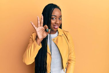 Genç Afro-Amerikalı kadın rahat bir ceket giyer ve üç numaralı parmaklarıyla gülümseyerek mutlu ve kendinden emin bir şekilde gösterir.. 