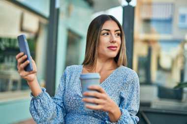 Genç İspanyol kadın şehirde akıllı telefon kullanarak mutlu bir şekilde gülümsüyor.