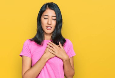 Güzel Asyalı genç bir kadın, sıradan pembe tişörtler giyiyor, elleri göğsünde, gözleri kapalı gülümsüyor ve yüzünde minnet ifadesi var. sağlık kavramı. 