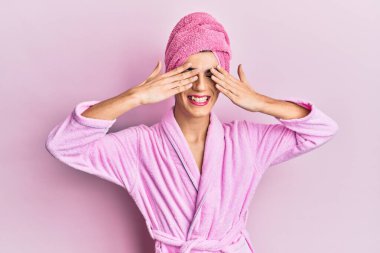 Kadın elbisesi giyen genç adam, duş havlusu ve bornoz giyip, elleri gülücüklü ve komik bir şekilde gözlerini kapatarak makyaj yapıyor. kör kavram. 