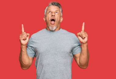 Orta yaşlı, gri saçlı, sıradan kıyafetler giyen, hayrete düşmüş, şaşırmış, parmaklarıyla işaret eden ve kollarını kaldıran bir adam.. 