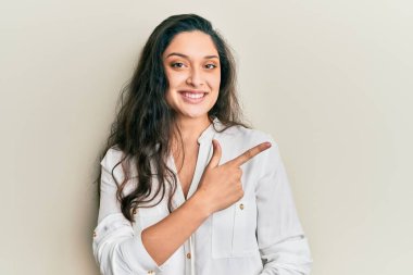 Güzel, orta doğulu, günlük kıyafetler giymiş neşeli, yüzünde mutlu ve doğal bir ifadeyle el ve parmak ile işaret eden bir gülümseme olan bir kadın. 